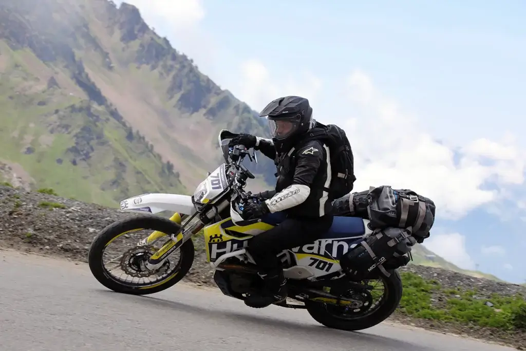 Husqvarna 701 Enduro fährt auf einer kurvigen Bergstraße mit beeindruckender Landschaft im Hintergrund.