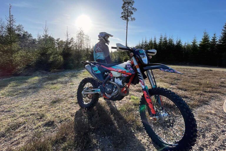 Motorradfahrer steht mit Motorrad im Wald.