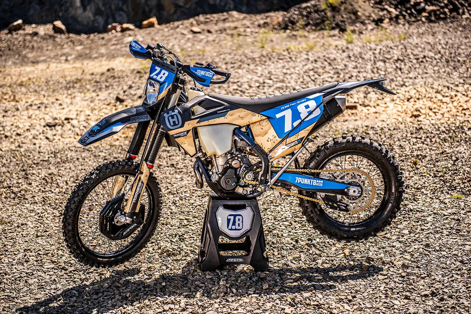 Blaues Husqvarna Motorrad mit Wüstenmuster und der Nummer 78 auf einem Schotterplatz.