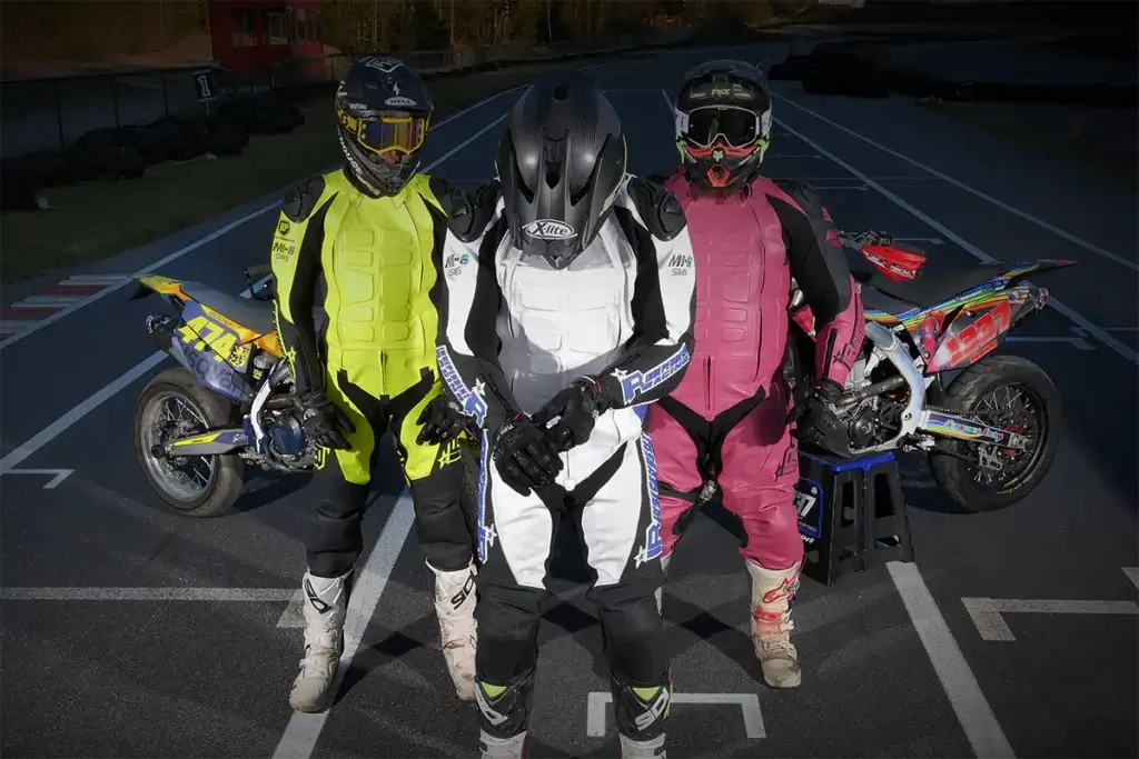 Drei Supermoto-Fahrer in bunten personalisierten Lederkombis auf Rennstrecke.