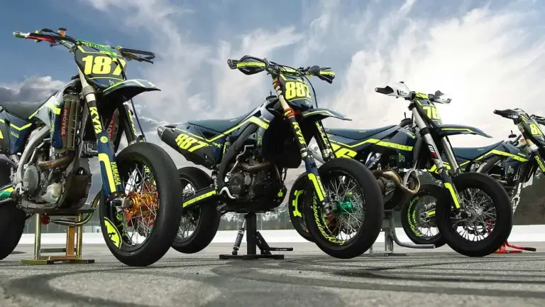 Vier Supermoto-Motorräder mit leuchtenden Dekoren von Independent Racing, aufgereiht vor einem dramatischen Himmel.