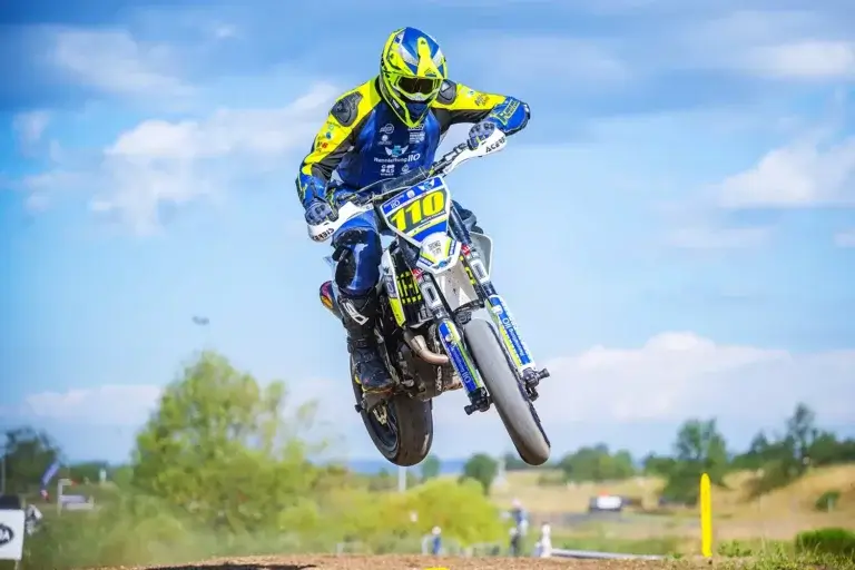 Fahrer in Polizei-Design Supermoto-Lederkombi springt mit Motorrad über Kuppe.