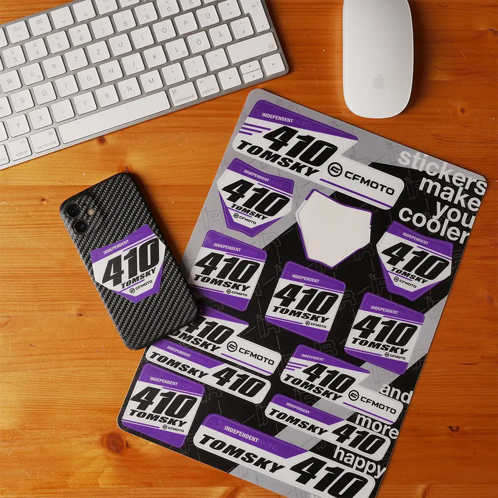 Individueller Rider ID Stickerbogen in Lila-Schwarz auf Holzschreibtisch, daneben Handy mit einem aufgeklebten Aufkleber.