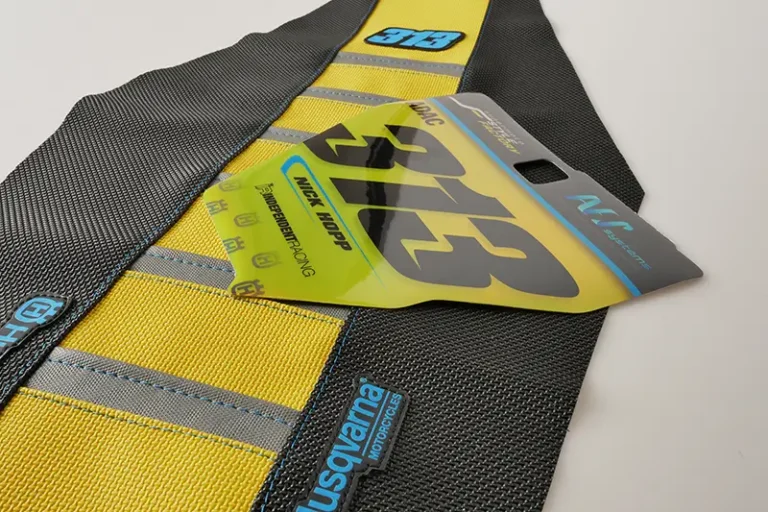 Gelb-schwarzer Sitzbankbezug mit grauen Rippen und Husqvarna-Logo, daneben eine gelbe Startnummerntafel.