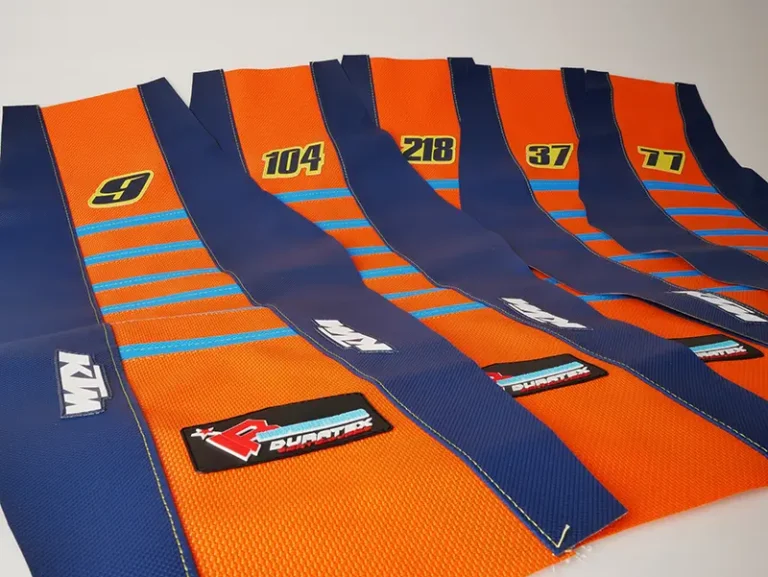 Mehrere orange-blaue Sitzbankbezüge mit KTM-Logo und aufgedruckten Startnummern.