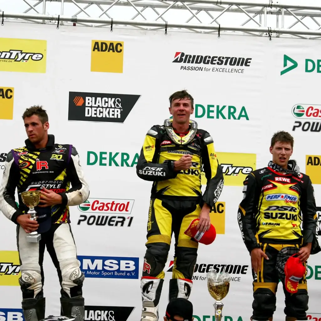 Fahrer auf dem Podium mit Independent Racing Lederkombi und Pokal.